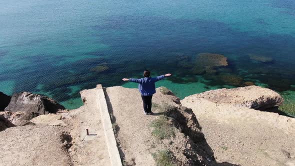 A Boy Stands Spreading His Arms on the Seashore the Sun Shines in His Face the Wind