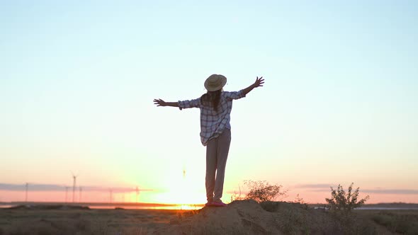 Silhouette Woman Tourist Stands in Front of Beautiful Sunset View with Open Arms in Meadow