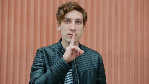Emotional Young Man Making Shush Gesture Asking for Silence Standing Outdoors