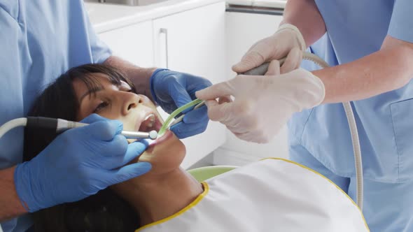 Hands of male dentist with dental nurse examining teeth of female patient at modern dental clinic