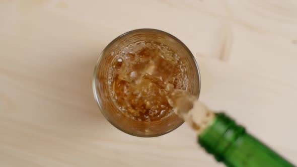 Top View Cold Rum or Whiskey Drink Pouring From Green Bottle in Glass With Ice Cubes Wooden Table