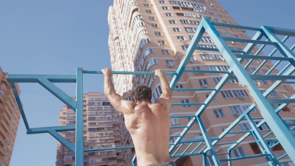 Athletic Man with Naked Torso Pulls Up on Horizontal Bar on Bright Sunny Day