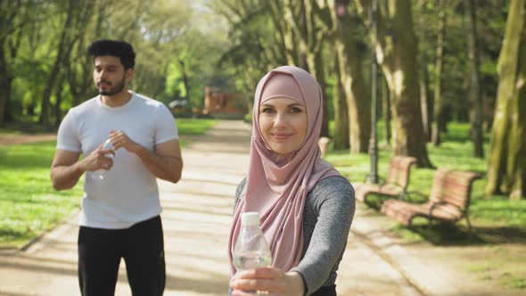 Pretty Woman in Hijab Holding Water of Bottle While Muslim Guy Standing Behind