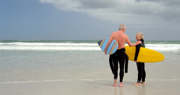 Old caucasian senior couple holding surfboard at beach 4k