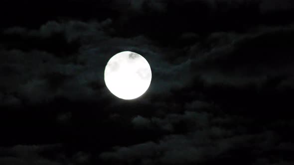 Moon time lapse as it rises into the night sky. Moon rising with clouds passing by for a spooky, eer