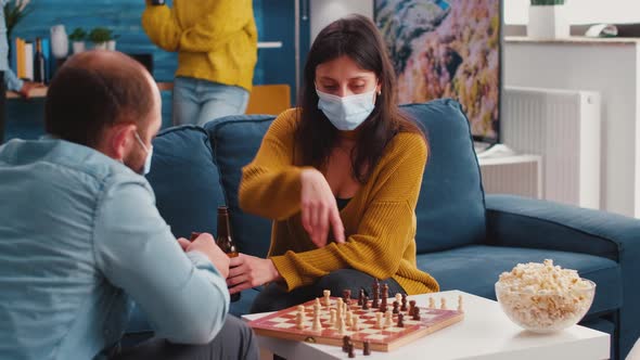 Focused Woman Wearing Face Mask Playing Chess with Man Friend