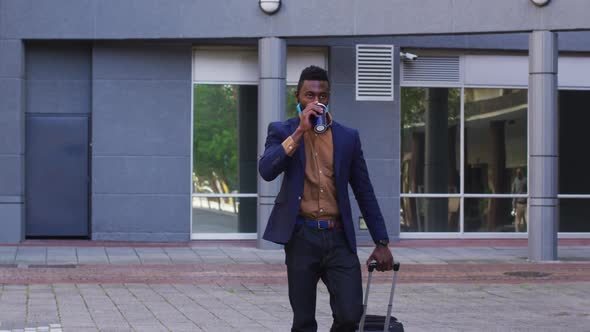 African american businessman with face mask walking drinking coffee in street