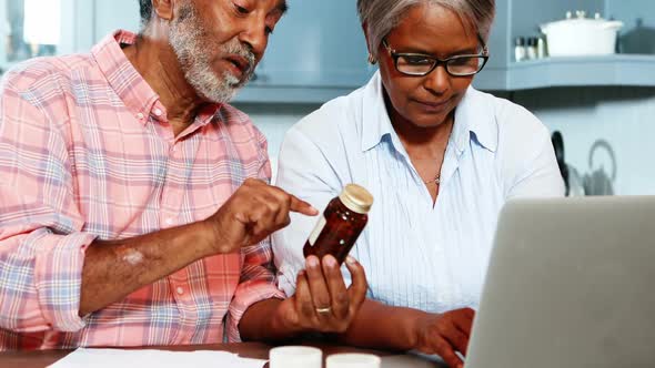 Senior couple holding medicine bottle and using laptop