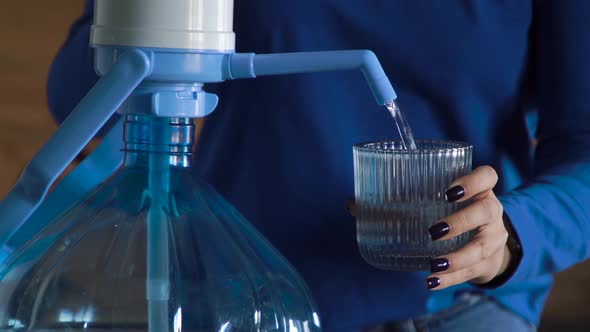 Woman Presses Pumps Water From a Large Bottle Into a Blue Glass at Home Kitchen