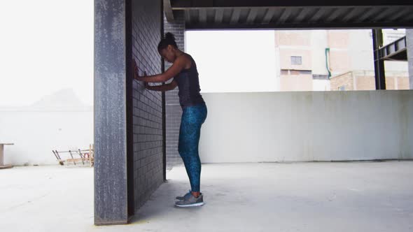 African american woman stretching leaning on a wall in an empty urban building