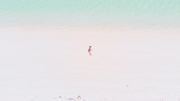 Aerial: Woman on white sand beach turquoise water tropical coastline caribbean sea