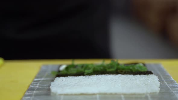 A cook is about to prepare a sushi roll with seaweed and mussels. He puts those ingredients on sushi