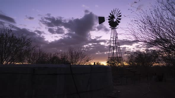 Timelapse of a windpump and water tank against a dramatic sunset with orange clouds transitioning in