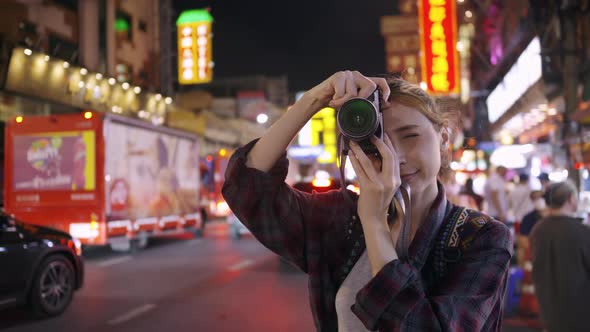 A female tourist enjoys taking photos of the night view of Yaowarat Road or Chinatown in Bangkok