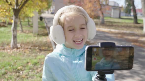 Happy Cute Little Vlogger Making Online Video Recording Vlog Sitting on a Park Bench. Record Vlog