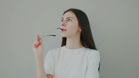 Millennial girl in white clothes holding glasses in hands looking around thoughtfully