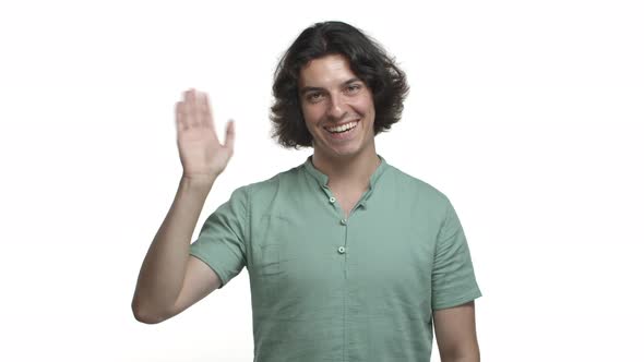 Handsome Hispanic Man in Green Shirt Saying Hello Smiling Friendly and Waving Hand to Greet you