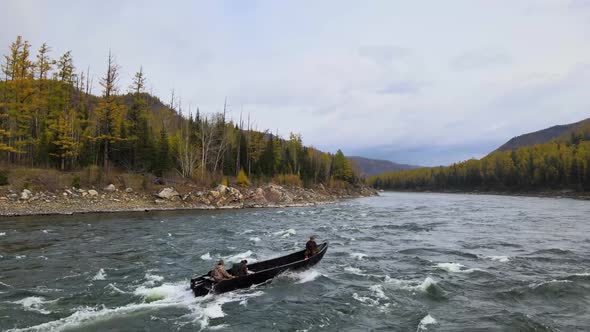 Several People in a Boat Float Along a Mountain River Around a Forest and Mountains