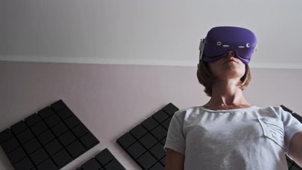 Young Woman in a VR Helmet Plays a Game at Home