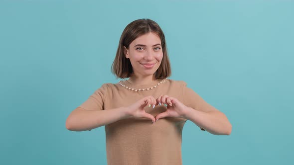 Happy Woman Put Make with Fingers Heart Shape, Isolated on Turquoise Background.