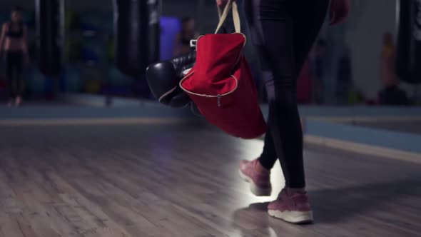 Closeup View of Legs of Young Fit Woman Entering a Fitness Club with a Bag and Boxing Gloves and