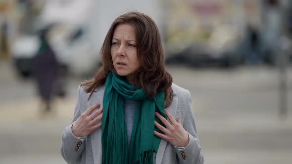 a Middleaged Brunette in a Gray Suit and with a Dissatisfied Face Adjusts a Turquoise Scarf Around