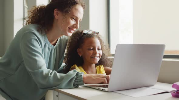 Video of happy caucasian female teacher explaining lesson on laptop to african american girl