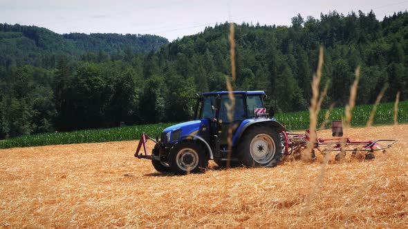 Tractor with trail working on wheat field, harvesting grain.