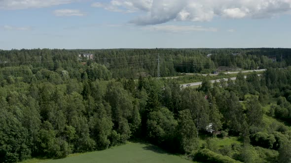 Slow aerial pan of a motorway in Finland near Kerava lined by powerlines and trees.