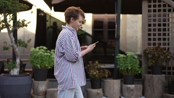 Live Camera Follows Happy Young Woman Messaging Online on Smartphone Walking on City Street in Slow