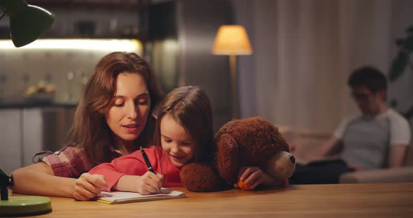 Mother and Little Daughter Doing Homework Together in Evening at Home