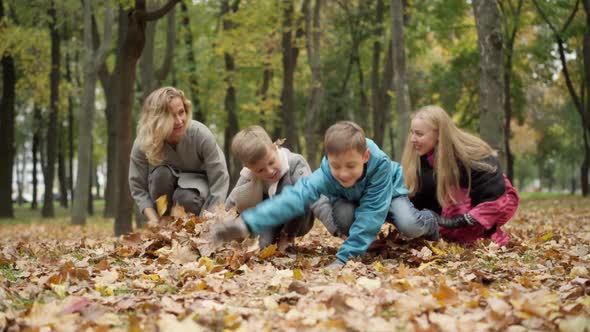 Wide Shot of Joyful Carefree Mothers and Sons Tossing Yellow Leaves in Autumn Park