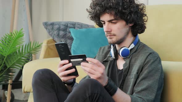 Curly Haired Man Shopping Online with Credit Card Using Smart Phone at Home