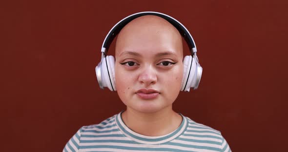 Bald young woman looking on camera while listening music playlist with wireless headphone