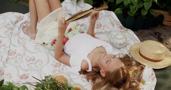 Cheerful Young Girl Lying and Reading Book in Garden