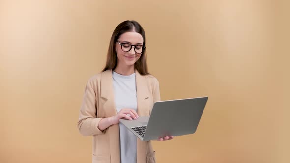 Young Woman Holding Laptop with a Smile Recommending Showing Positive Feedback Over a Beige