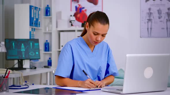 Medical Assistant Typing on Laptop and Taking Notes on Clipboard