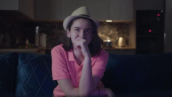 Teenage Girl in a Hat Watching a Movie at Night and Smiling Sitting on the Couch