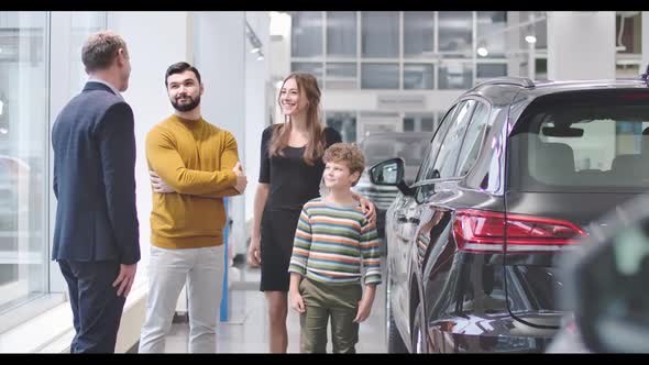Four Caucasian People Standing Next To New Automobile in Car Dealership