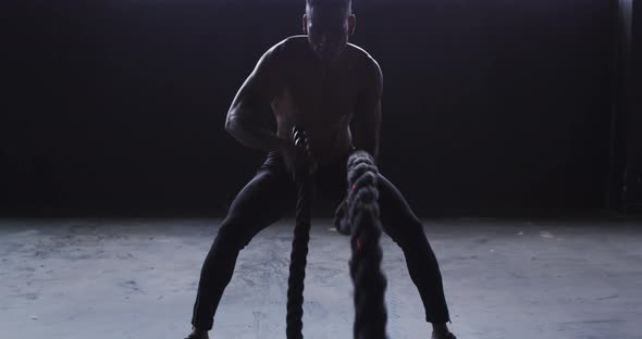 Shirtless african american man exercising battling ropes in an empty building