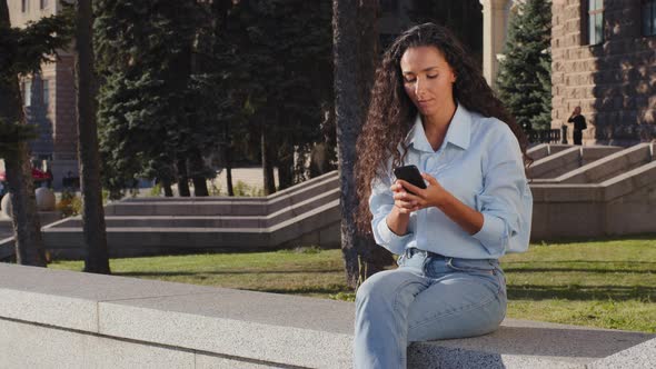 Young Beautiful Brunette Girl Woman Smiling Waiting Sitting in City Street Looking at Mobile Phone