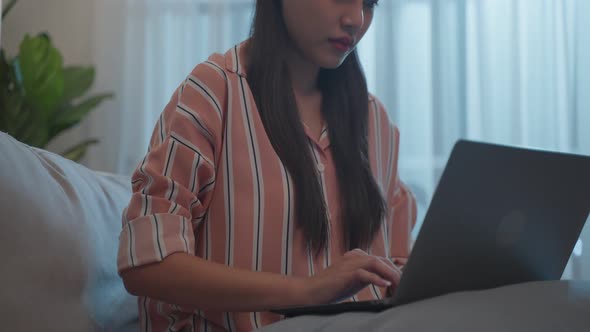 Asian beautiful girl typing on laptop keyboard in living room at night.