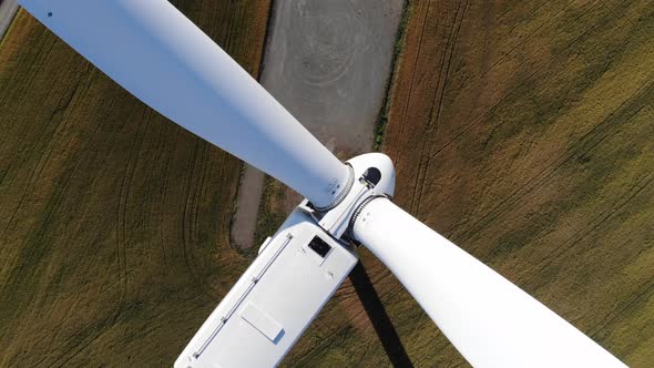 Top down aerial view, flying in-between the blades of a wind turbine in the middle of the wind farm
