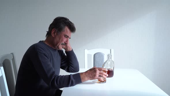 Depressed Mature Man Drinking Alcohol at Table