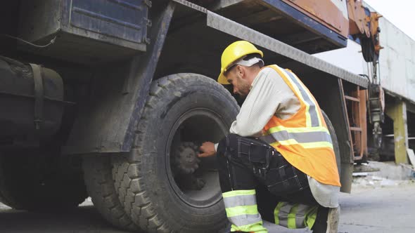 Portrait of Young Mechanic in Work Clothes and Hardhat Checking Construction Vehicles Tires