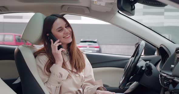 Young Woman in Beige Coat Talking on the Phone While Sitting in the Car
