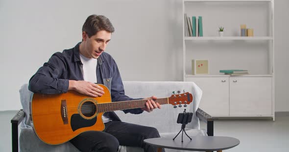 Caucasian Young Male Talented Musician Uses Mobile Phone to Record Guitar Playing Speaks Into