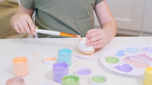 A Small Child Paints a White Chicken Egg in Beige Using a Drawing Bone