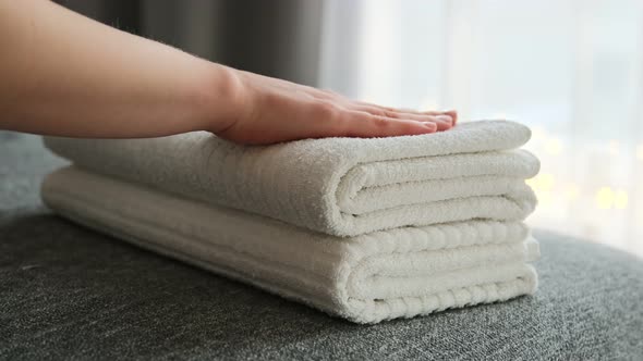 Woman hands putting stack of fresh clean white bath towels on the bed.