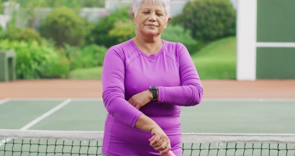 Video of happy biracial senior woman holding racket on tennis court